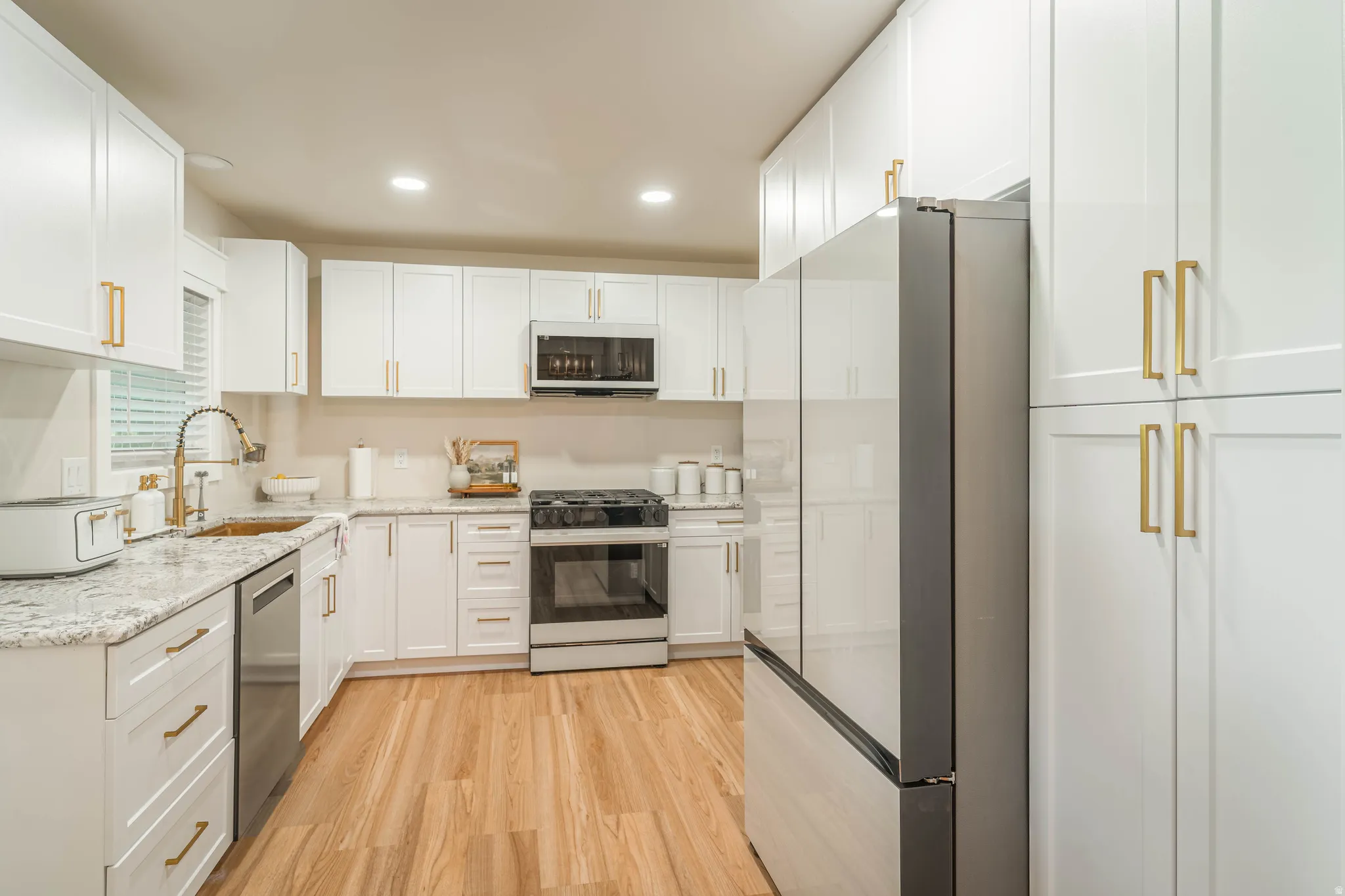 Modern kitchen featuring crisp white cabinetry with brushed gold hardware, granite countertops, and a subway tile backsplash
