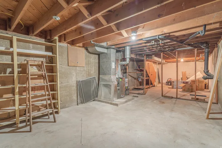 Spacious basement featuring exposed wood beam ceiling, concrete flooring, and multiple framed wall sections ready for customization