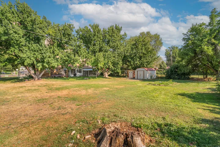 Expansive residential lot featuring mature shade trees, open lawn space, and detached outbuildings