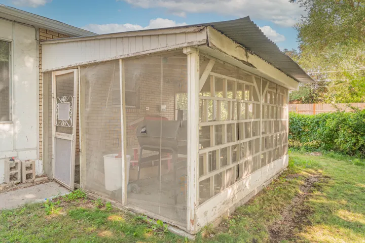 Screened outdoor room with wood-frame construction and mesh paneling, offering shelving storage and direct access to the main residence