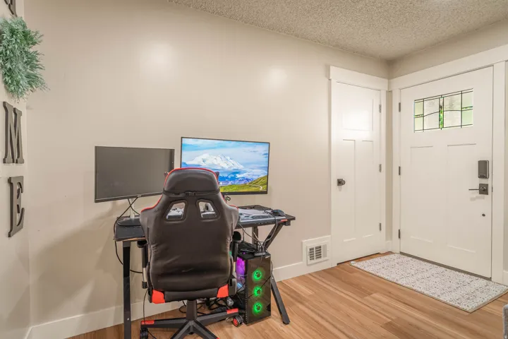 Dedicated home office featuring hardwood flooring, dual monitor setup with professional gaming chair, and abundant natural light from street-facing windows