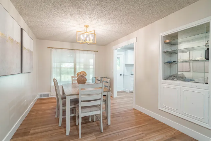 Dining room featuring wood-finish flooring, a white painted dining table with ladder-back chairs, and a white built-in display cabinet with glass doors