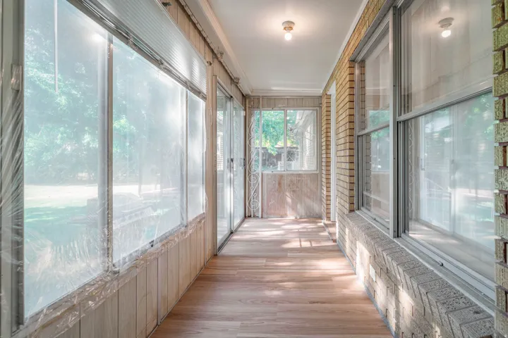 Sunlit enclosed porch featuring expansive windows, wood-finish flooring, brick exterior detailing, and recessed ceiling lighting