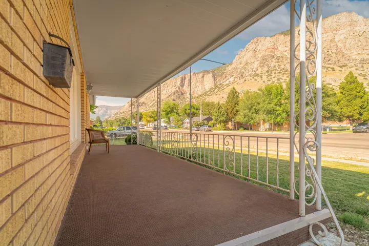 Covered porch with decorative wrought-iron railings and brick exterior, overlooking manicured lawn and mature landscaping framed by mountain backdrop