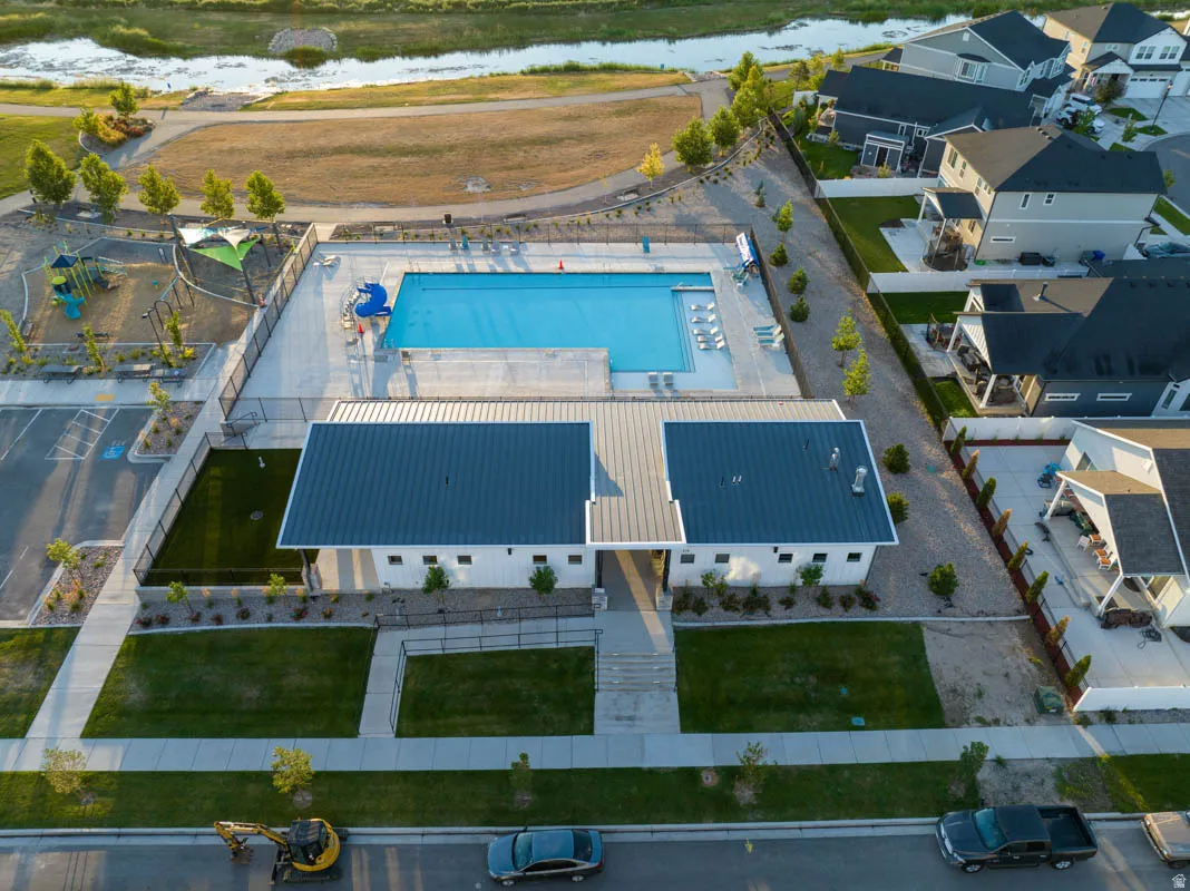 Community building with a dark metal roof and white siding, outdoor swimming pool with water slide, adjacent playground, and nearby open green spaces