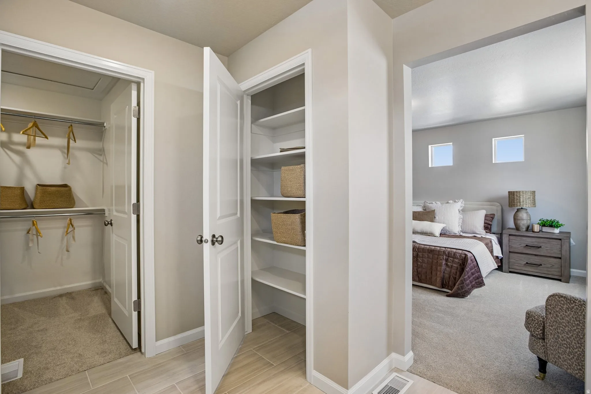 Recessed shelving unit, walk-in closet with carpeted flooring, and a bedroom featuring carpeted flooring and two square windows