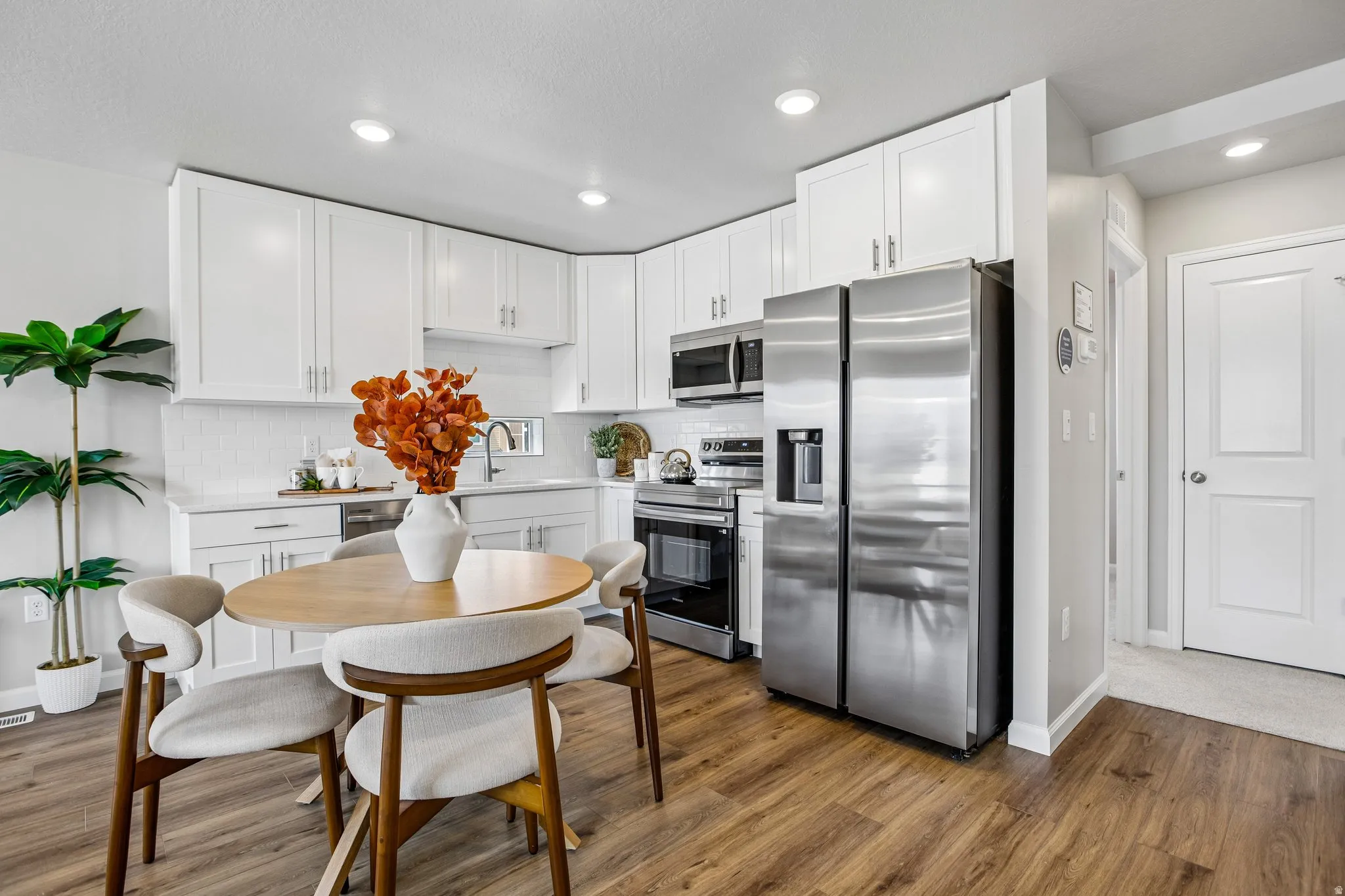 White shaker cabinetry, stainless steel appliances, white subway tile backsplash, recessed lighting, and wood-finish flooring