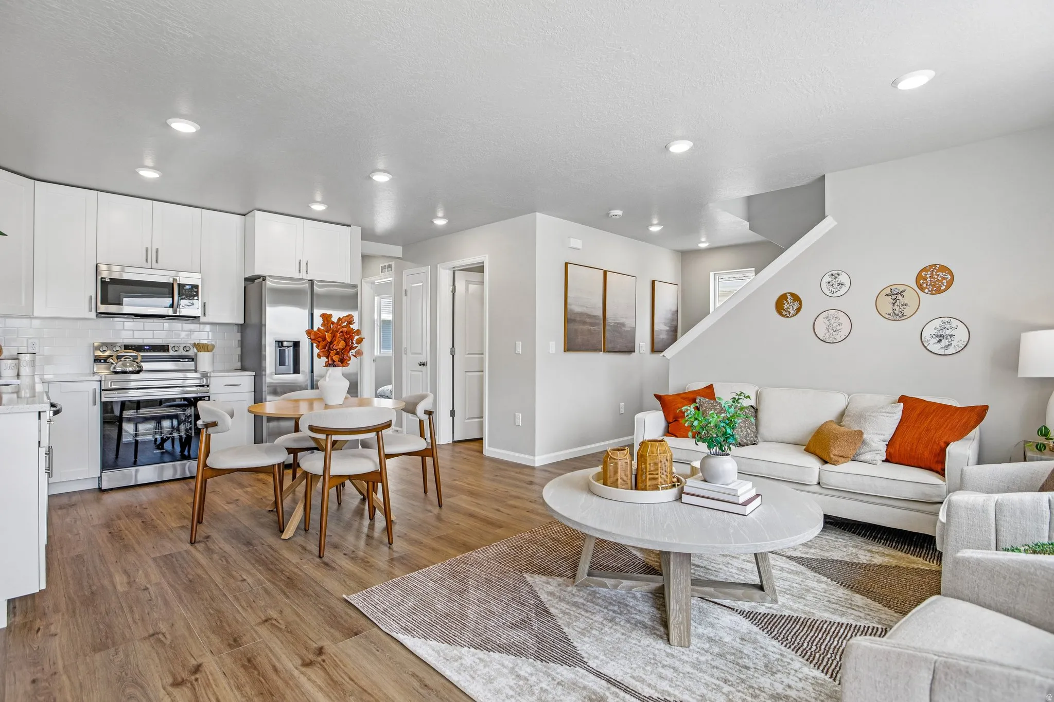 Open-concept living space with wood-finish flooring, recessed lighting, and a modern kitchen featuring white cabinetry, stainless steel appliances, and a subway tile backsplash