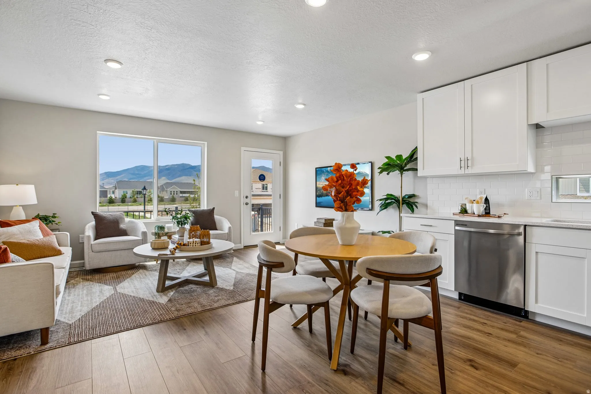 Open-concept design featuring wood-finish flooring, recessed lighting, and a kitchen with white cabinetry, a subway tile backsplash, and stainless steel appliances