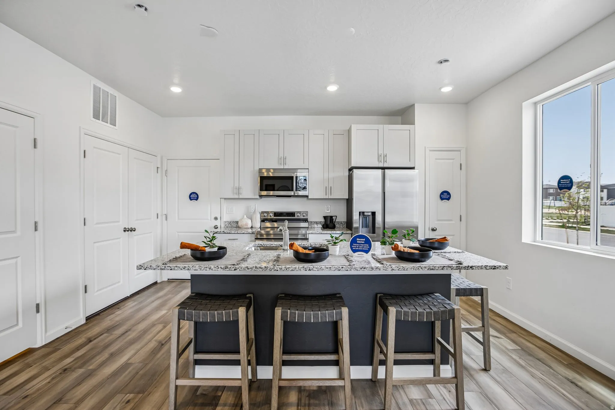 Kitchen featuring an island with a stone countertop, white cabinetry, stainless steel appliances, and wood-finish flooring
