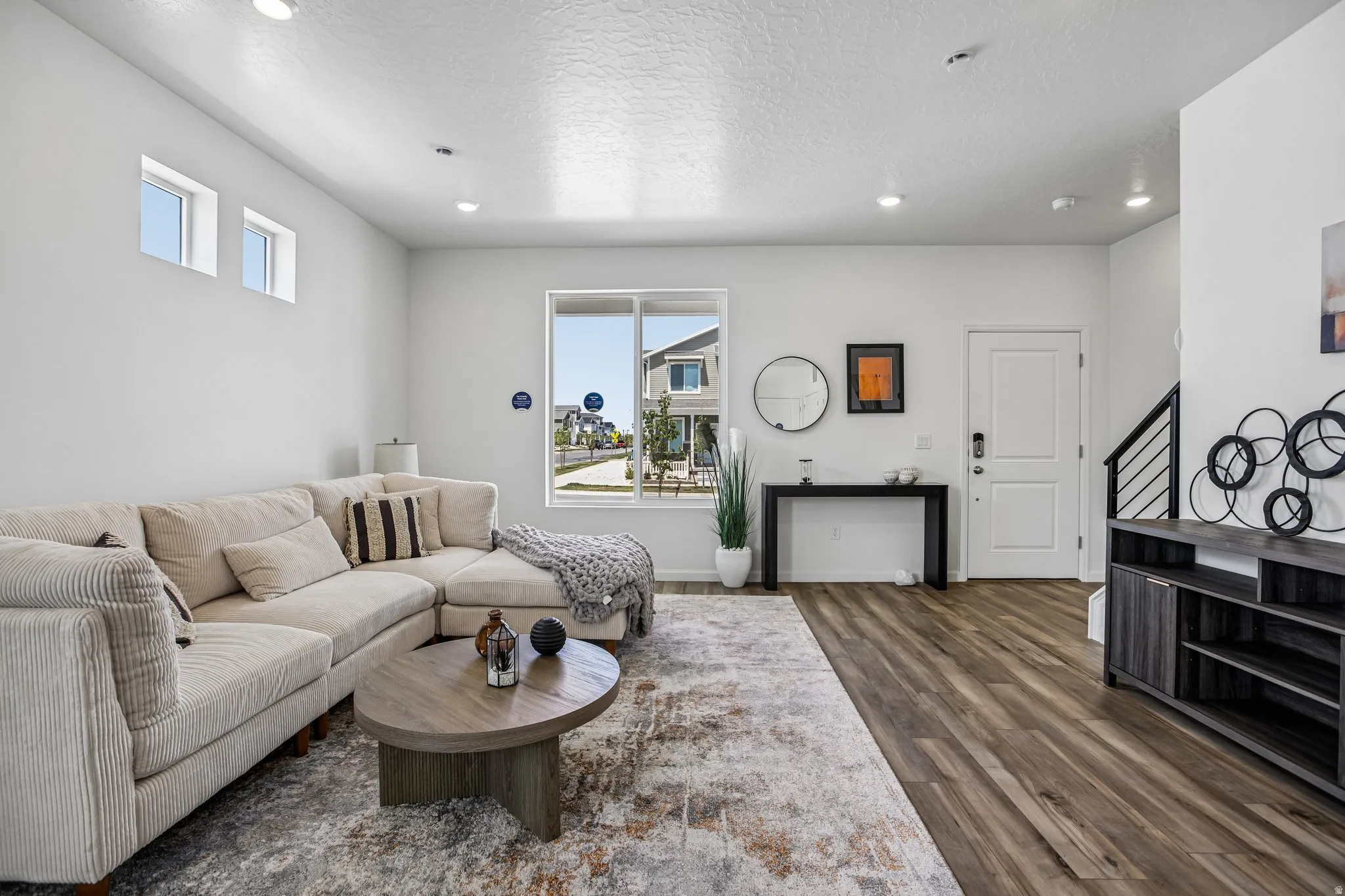 Recessed ceiling lighting, wood-finish flooring, white paneled door, and a black metal staircase railing