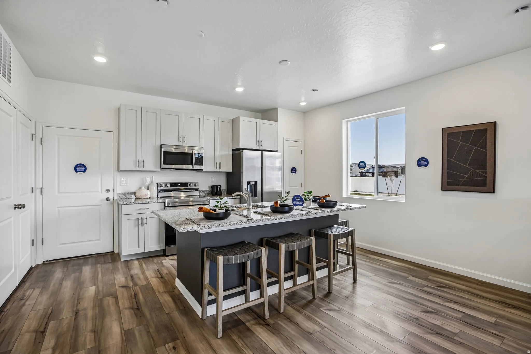 Kitchen featuring an island with seating, stainless steel appliances, light gray cabinetry, wood-finish flooring, and a large window