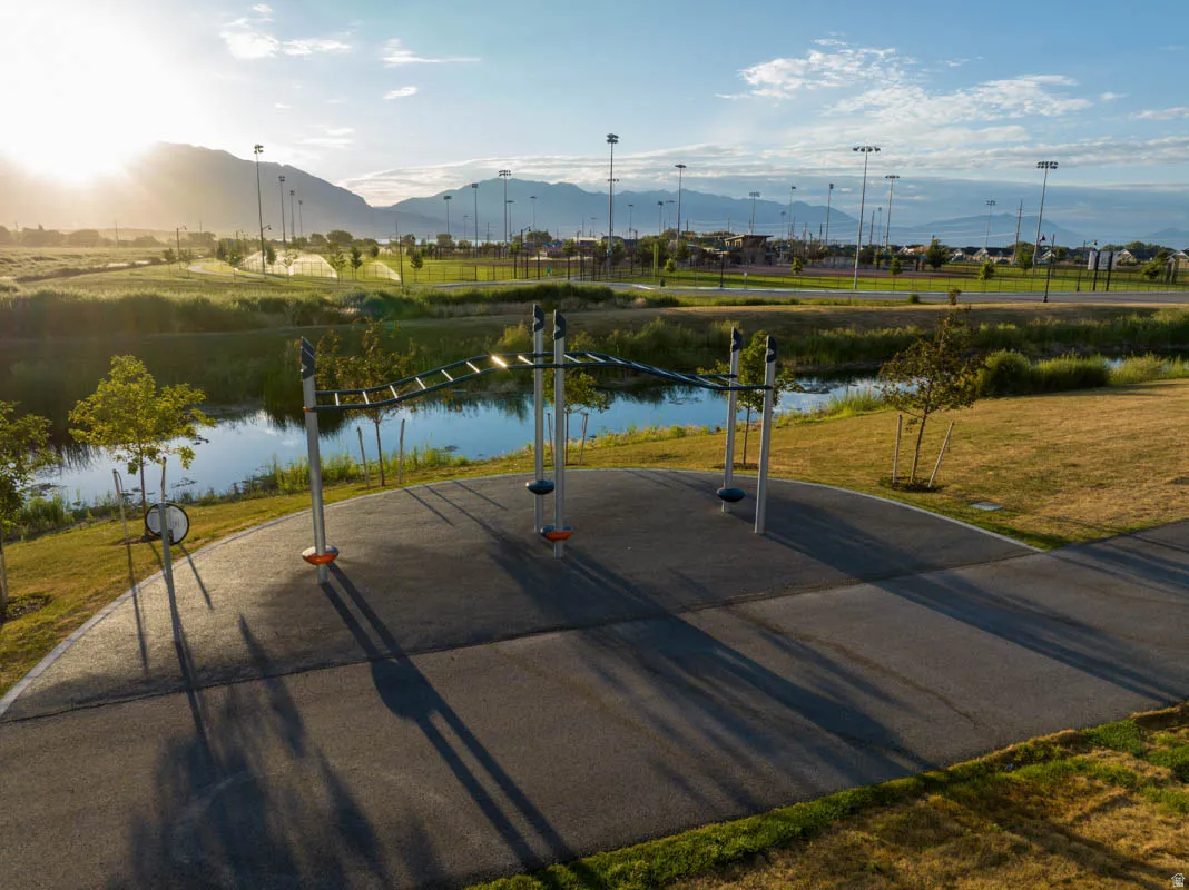Outdoor fitness equipment, paved pathway, natural water feature, manicured grass, distant mountains