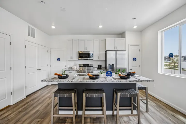 Kitchen featuring an island with a stone countertop, white cabinetry, stainless steel appliances, and wood-finish flooring