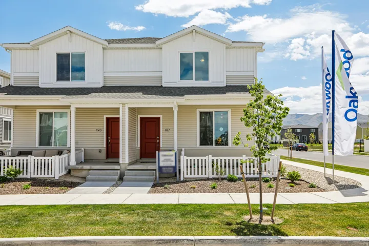 Contemporary duplex featuring red entry doors, light-colored siding, white window trim, and a white picket fence enclosing a front patio area