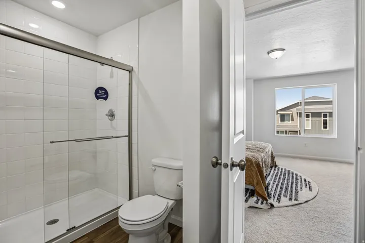 Glass-enclosed shower with white subway tile surround, wood-finish flooring, and recessed lighting