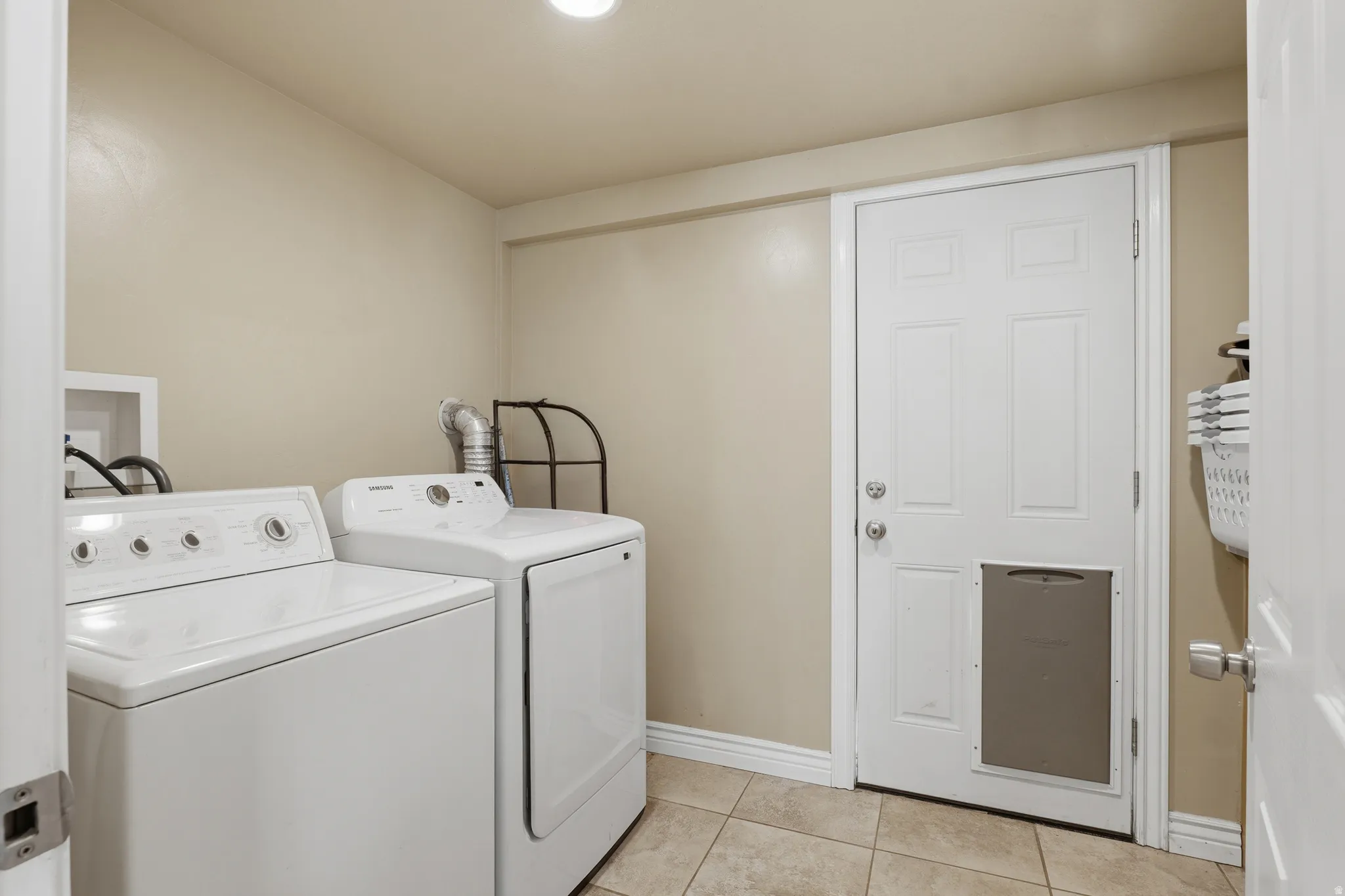 Dedicated utility space featuring a washer and dryer, finished with tiled flooring, and a panel door with a built-in pet door