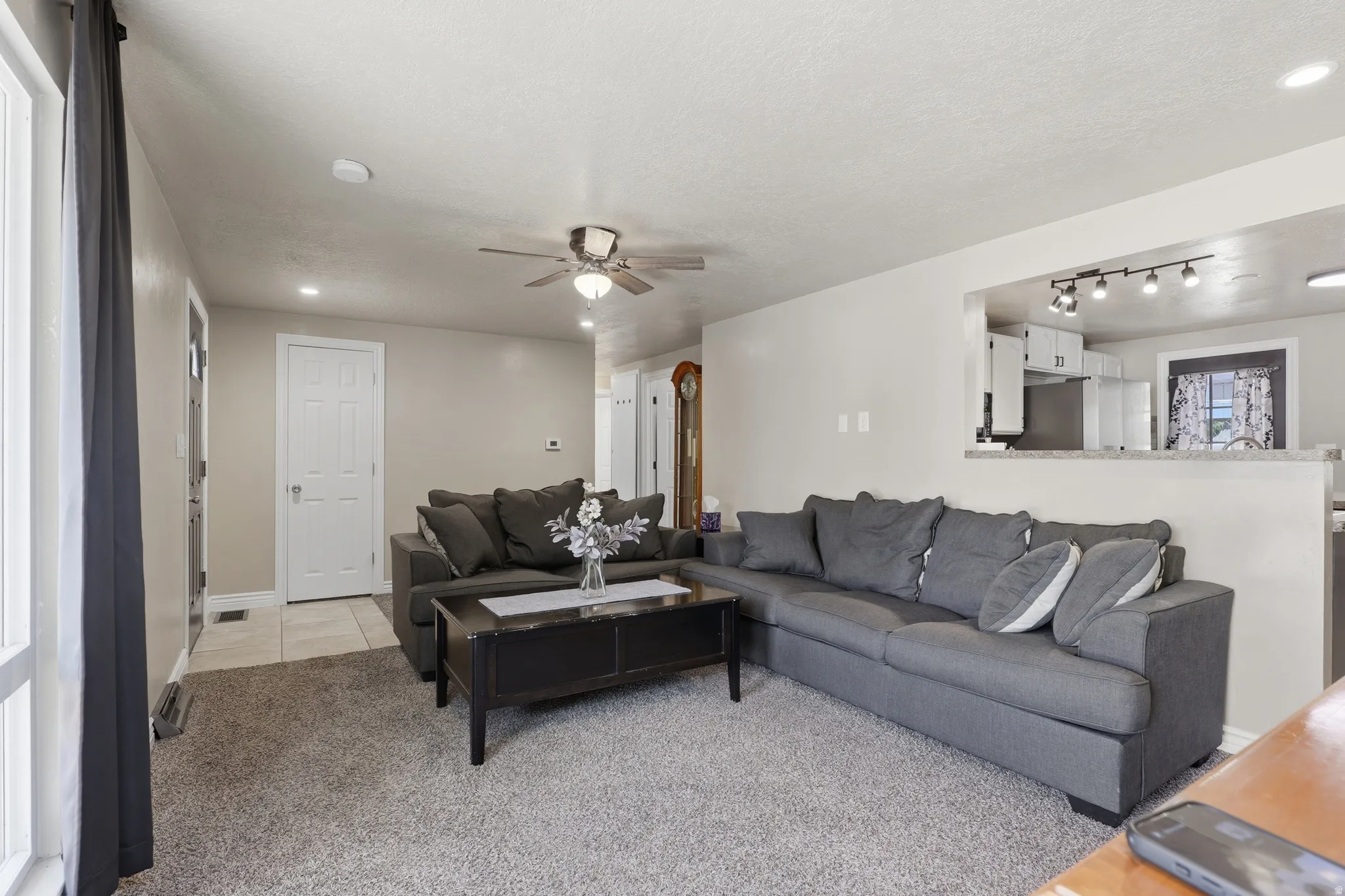 Recessed lighting, ceiling fan, carpet flooring, and a pass-through opening to the kitchen