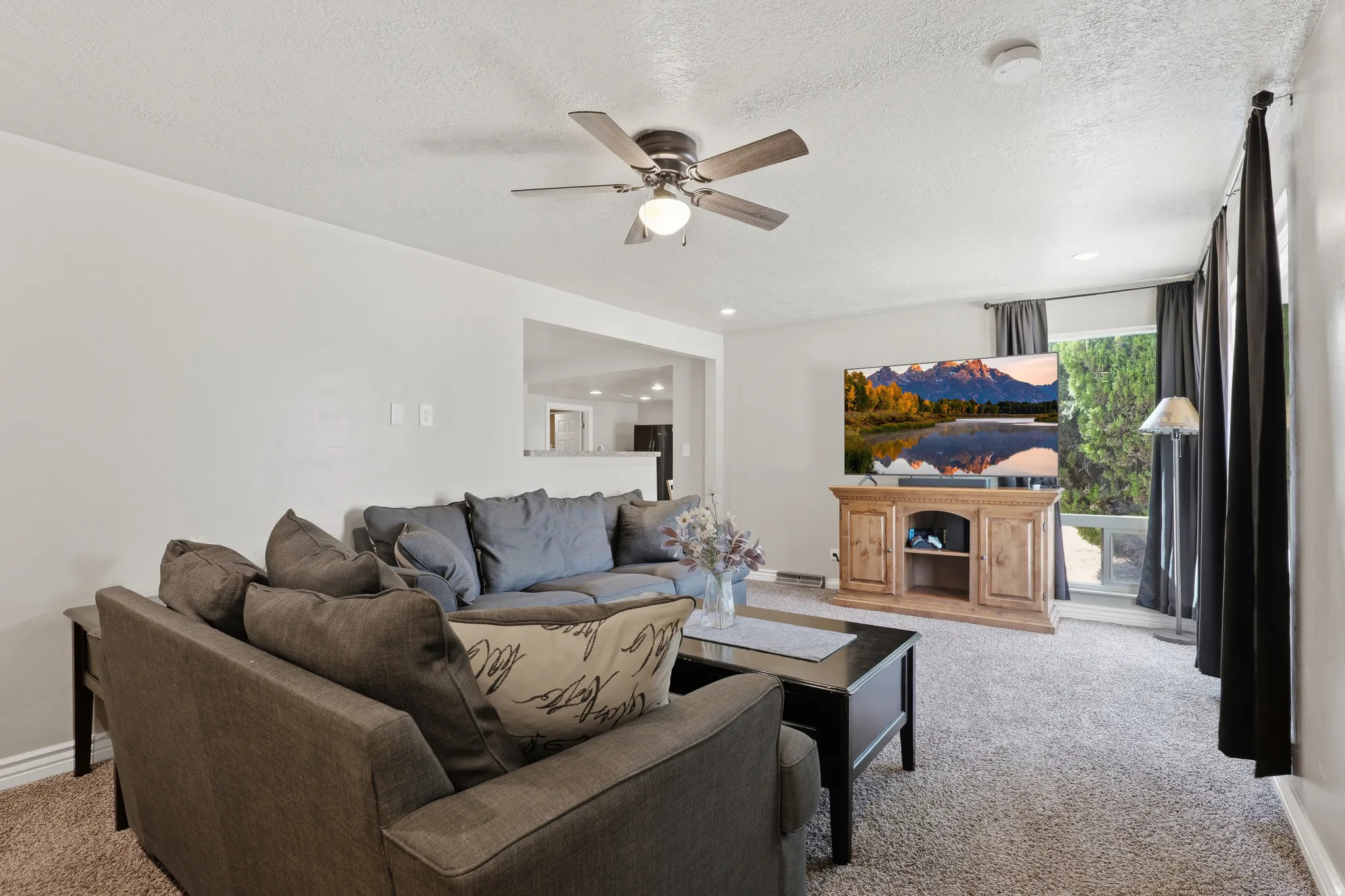 Recessed lighting, wood-finish ceiling fan, wall-to-wall carpeting, and a window with dark drapery panels