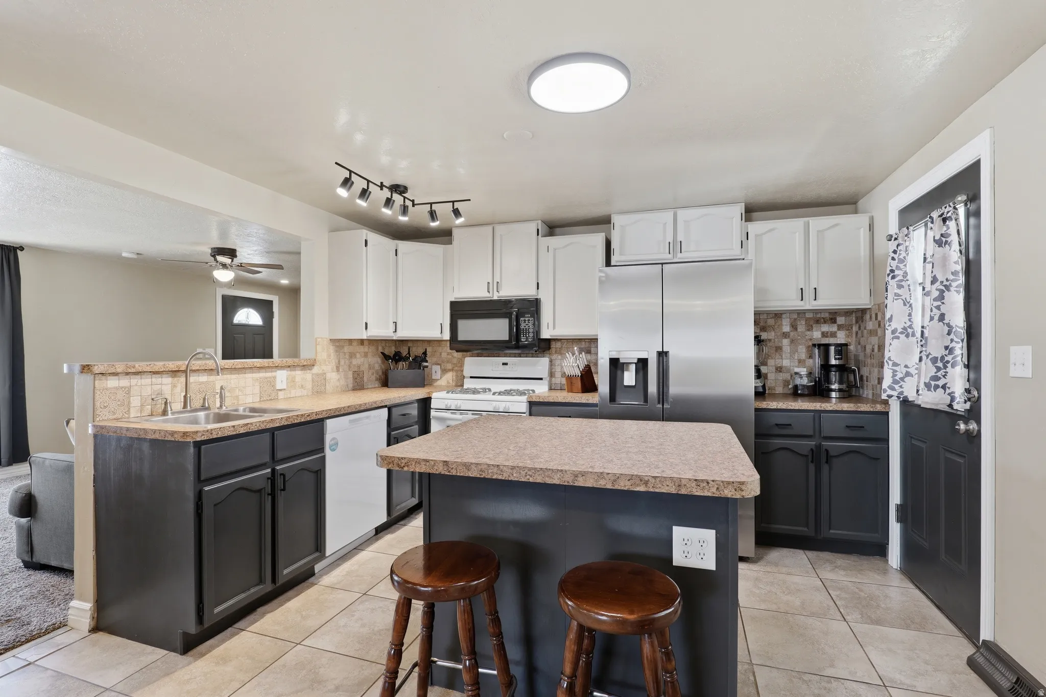 Kitchen featuring a two-tone cabinetry design, tiled flooring, integrated stainless steel appliances, a center island with counter seating, and a matching tiled backsplash