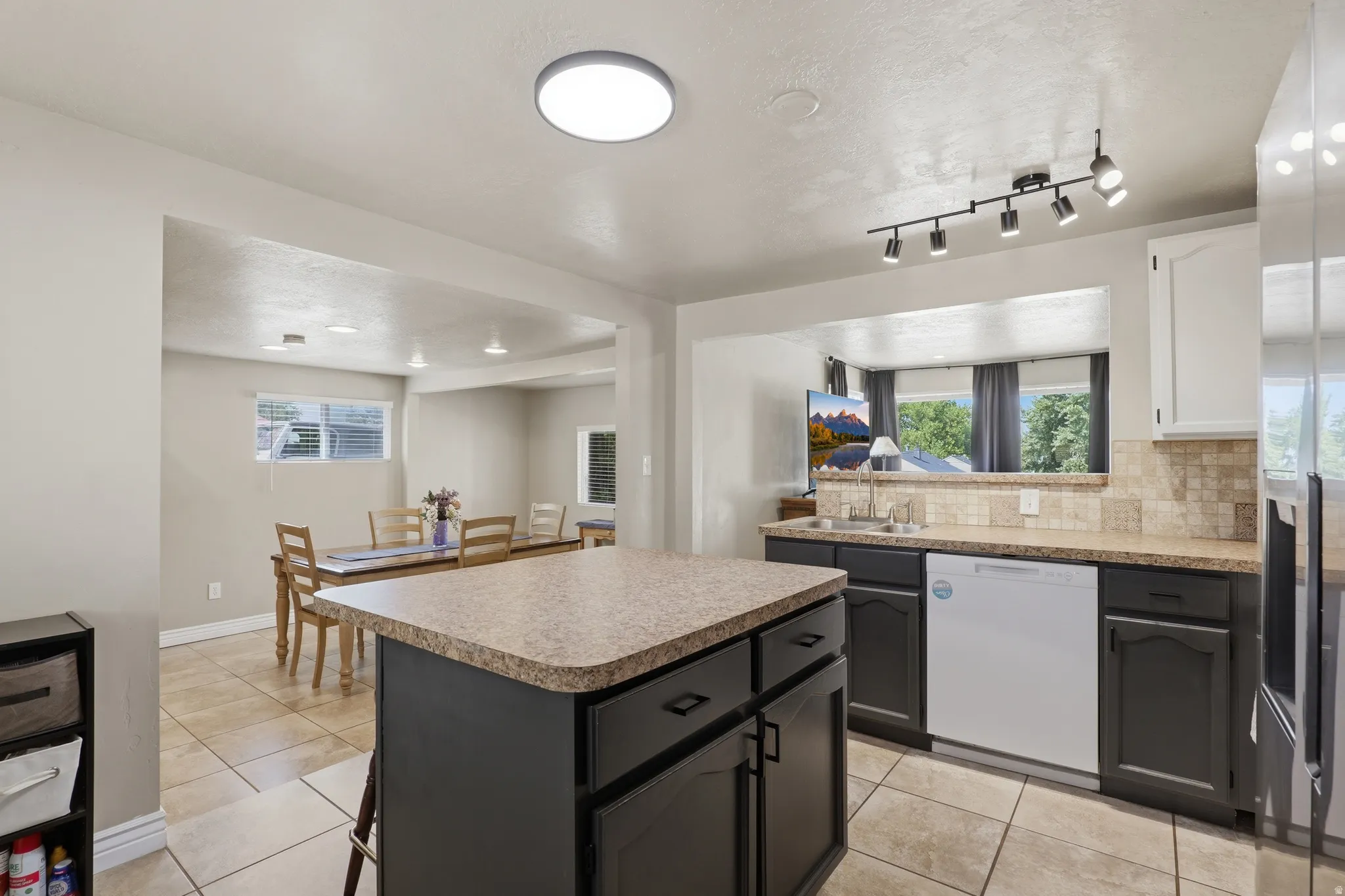 Kitchen featuring an island with built-in cabinetry, tile flooring, track lighting, and a window above the sink