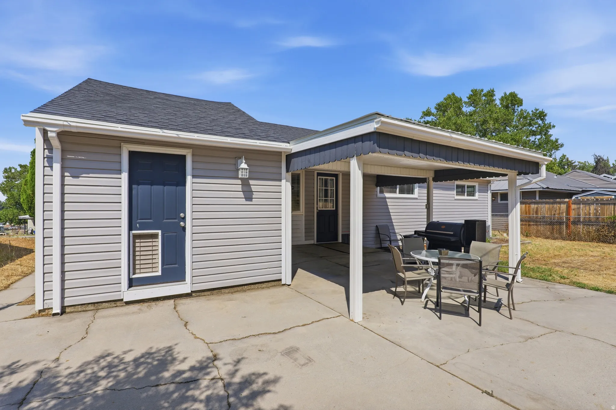 Covered patio with a dark grey shingled roof, light grey siding, and a dark blue entry door