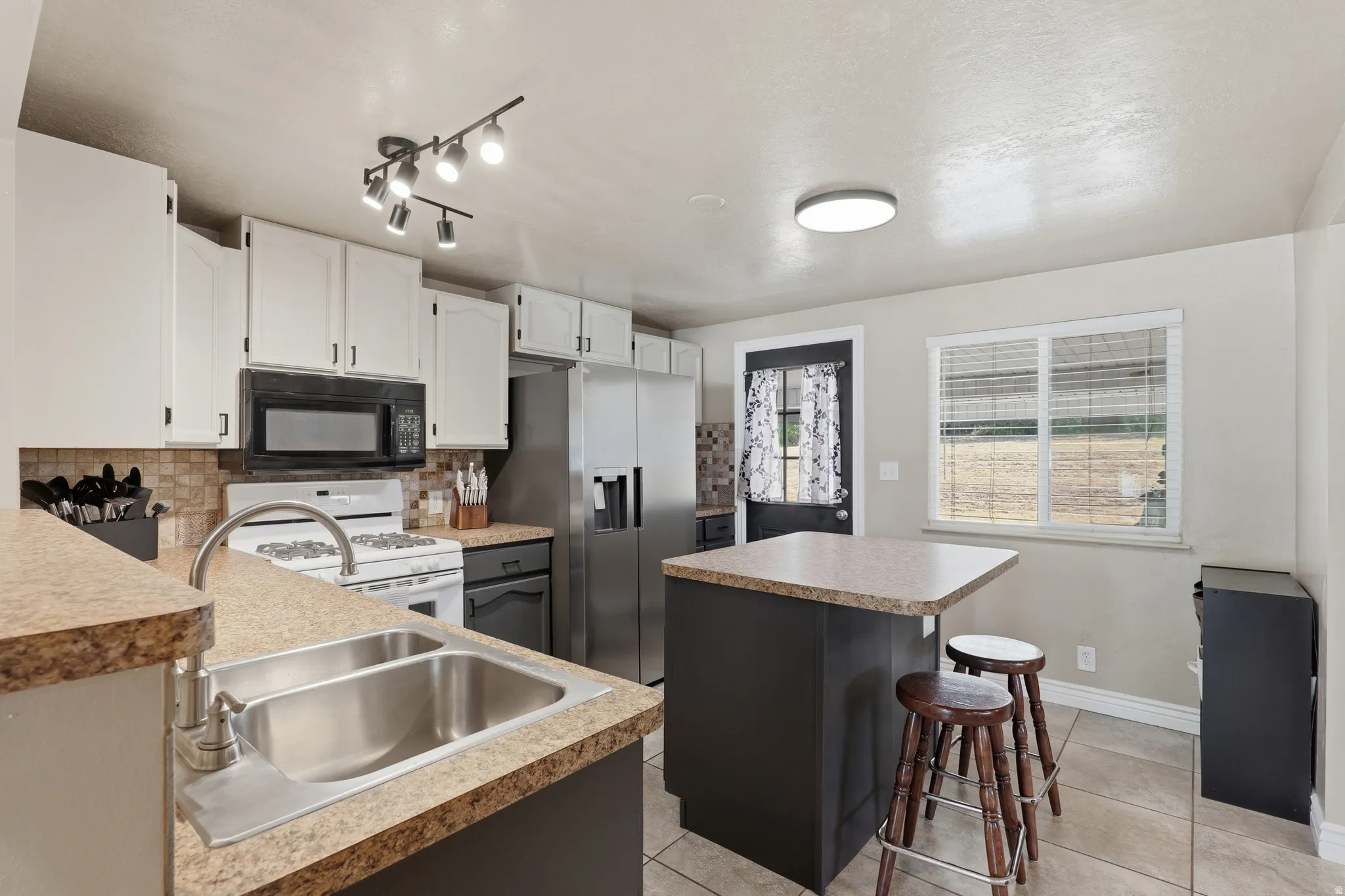 Kitchen featuring white cabinetry, a dual basin stainless steel sink, stainless steel appliances, and a central island with countertop space