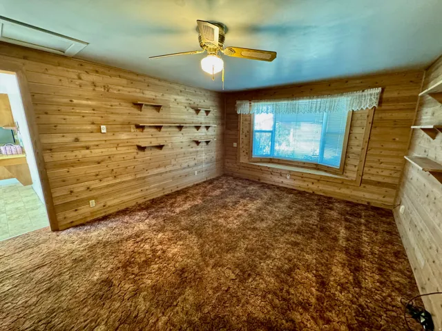 Wood-paneled interior walls, built-in shelving, bay window, ceiling fan, and carpeted flooring