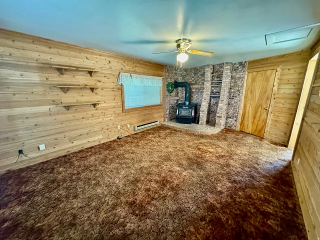 Wood paneling walls with built-in shelving, a brick fireplace with a wood-burning stove, and a ceiling fan