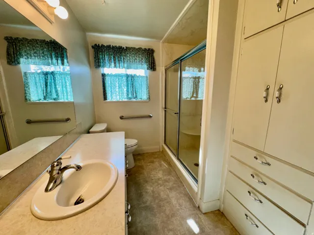 Integrated vanity with undermount sink, mirrored wall, toilet, shower enclosure with sliding glass door, and built-in cabinetry with drawers