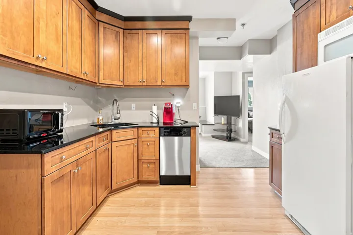 Kitchen featuring wood-finish cabinetry, dark countertops, a stainless steel dishwasher, and wood-finish flooring