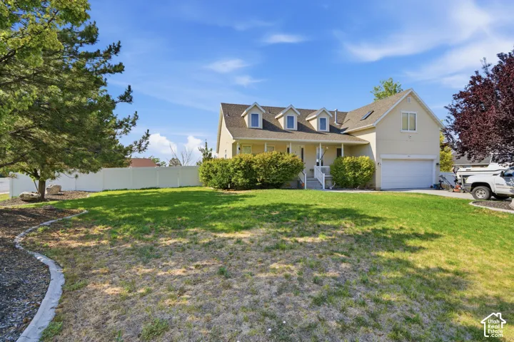 Gable roofline with three dormer windows, covered front porch, attached garage, and a lush front lawn with mature trees and shrubs
