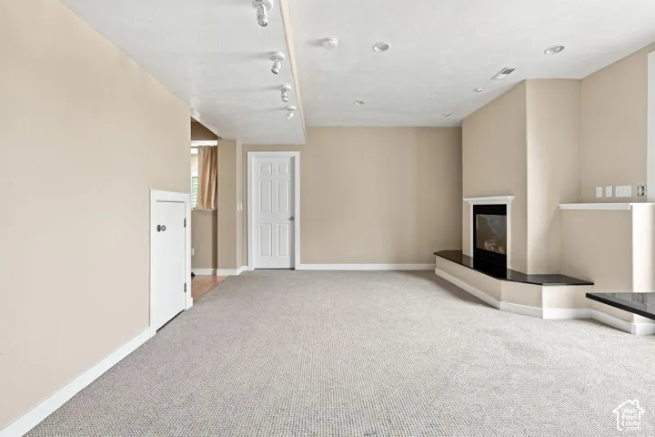 Recessed lighting, track lighting, built-in fireplace, black countertop, and neutral carpeting