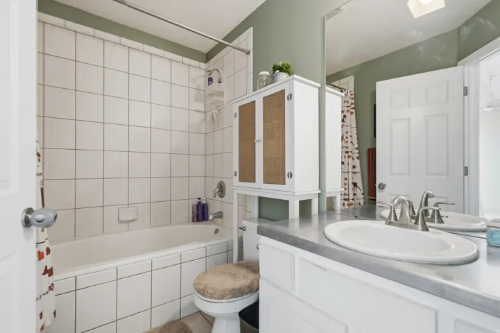 Bright bathroom featuring white subway tile surround, dual vanity with gray countertop and brushed nickel faucet, oval vessel sink, white cabinetry with wood-finish accents, and a separate soaking tub with tile enclosure and glass shower door