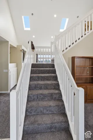 Staircase with carpeted treads and white wood railings, featuring two ceiling skylights and recessed lighting