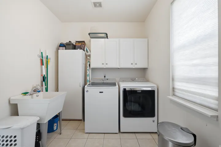 Laundry area with ceramic tile flooring, upper cabinetry, and a utility sink