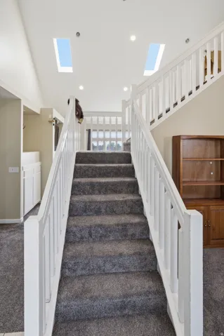 Staircase with carpeted treads and white wood railings, featuring two ceiling skylights and recessed lighting