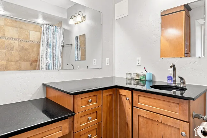 Built-in wooden vanity with ample storage, black countertop, integrated sink, and large wall-mounted mirror