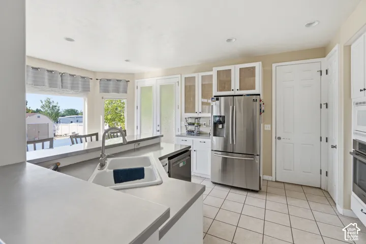 Kitchen with white cabinetry, stainless steel appliances, a double basin sink, light-toned countertops, and tiled flooring