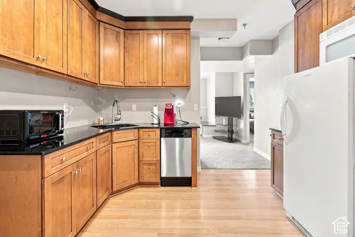Kitchen featuring wood-finish cabinetry, dark countertops, a stainless steel dishwasher, and wood-finish flooring