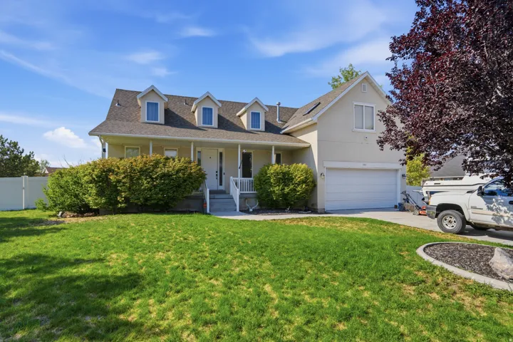 Multi-level residence featuring a dormer roofline, covered porch, attached garage, and mature landscaping