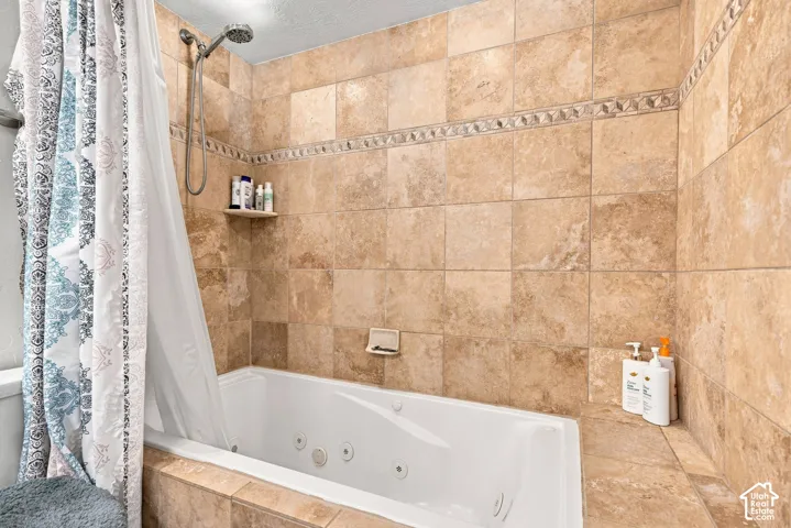 Built-in jetted tub surrounded by large format tile, decorative tile accent band, and a wall-mounted shower head with handheld attachment