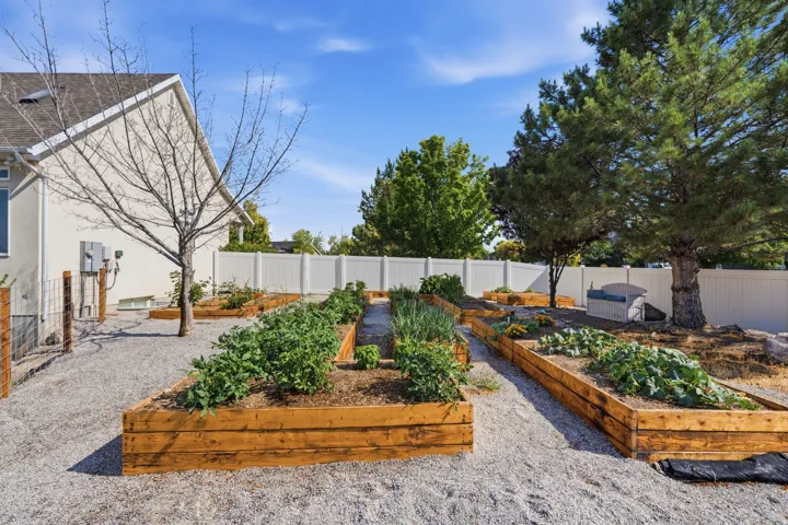 Expansive backyard featuring multiple raised garden beds, a white privacy fence, and mature trees