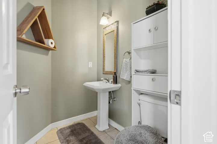 Pedestal sink, ceramic tile flooring, built-in storage cabinetry, wall-mounted mirror, and overhead vanity lighting