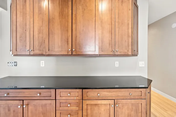 Wood-finish cabinetry with silver-tone hardware, dark countertop, and light wall paint