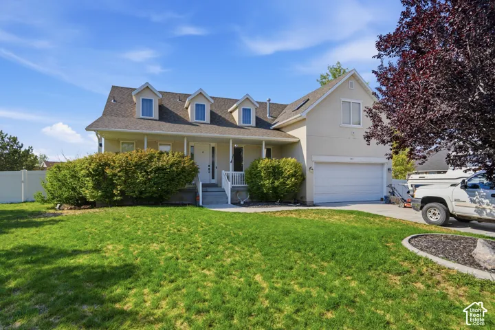 Multi-level residence featuring a dormer roofline, covered porch, attached garage, and mature landscaping