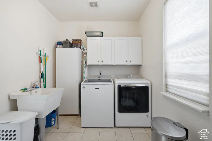 Laundry area with ceramic tile flooring, upper cabinetry, and a utility sink