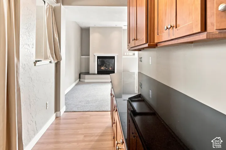 Warm wood cabinetry with dark countertops, wood-finish flooring, and a fireplace with a mantel