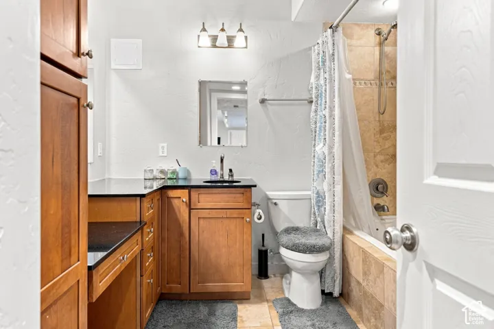 Bathroom featuring a built-in wood-finish vanity with black countertops, a wall-mounted mirror, a tub-shower combination with tiled surround, and ceramic tile flooring