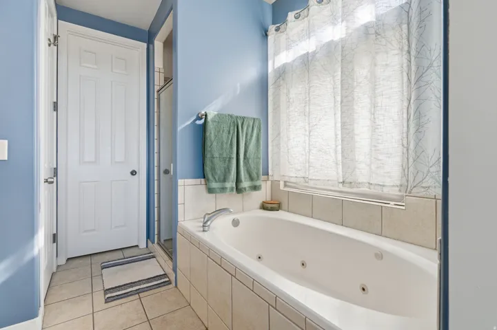 Built-in jetted tub with tile surround, glass-enclosed shower, and tiled flooring